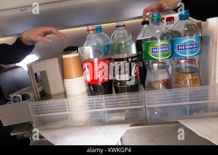 A drink trolley in the aisle on an Embraer 190 plane / aeroplane / airplane. Cabin crew are serving soft drinks to passengers during a flight. Stock Photo