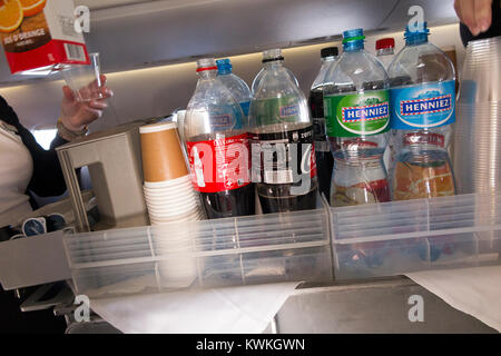 A drink trolley in the aisle on an Embraer 190 plane / aeroplane / airplane. Cabin crew are serving soft drinks to passengers during a flight. Stock Photo