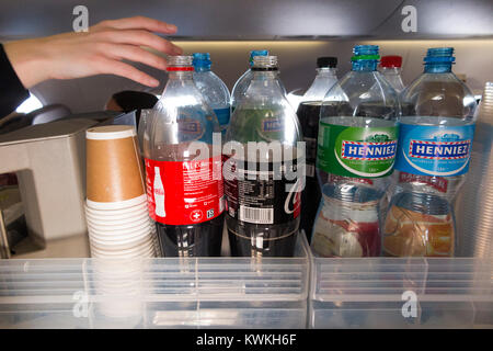 A drink trolley in the aisle on an Embraer 190 plane / aeroplane / airplane. Cabin crew are serving soft drinks to passengers during a flight. Stock Photo