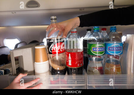 A drink trolley in the aisle on an Embraer 190 plane / aeroplane / airplane. Cabin crew are serving soft drinks to passengers during a flight. Stock Photo