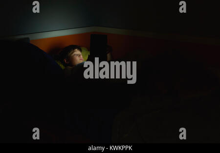 Boy using tablet computer while lying on bed in darkroom at home Stock Photo