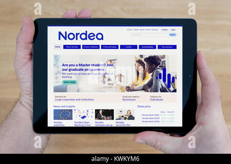 A man looks at the Nordea bank website on his iPad tablet device, over a wooden table top background (Editorial use only) Stock Photo