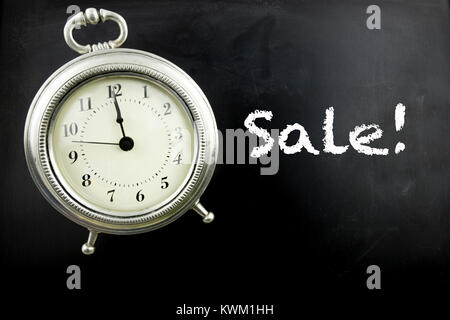 Pewter antique alarm clock on blackboard with Sale in white chalk. Stock Photo
