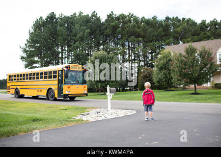 Rear view of boy with backpack waiting for school bus on road Stock Photo