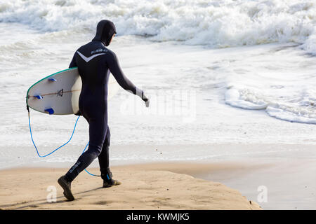 Bournemouth, Dorset, England UK. 4th January, 2018. UK weather:  surfer holding surfboard, heading into the sea to enjoy the surf on a windy day at Bournemouth beach, as the surfers make the most of the windy conditions and big waves. Stock Photo