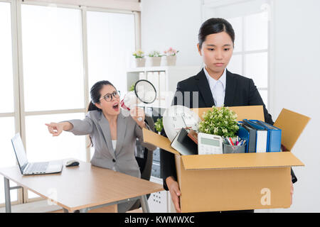 young beautiful business girl holding personal belongings box ready to leave company when angry mad boss woman using megaphone talking blame and fired Stock Photo