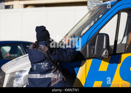 A female parking enforcer issues a ticket to an illegally parked van and places a ticket on the screen, uk Stock Photo