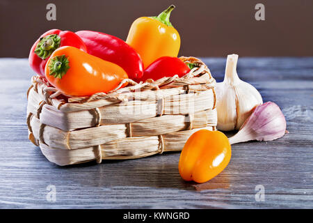 Red and yellow sweet pepper on a wooden table. Wattled straw box, close up, selective focus Stock Photo