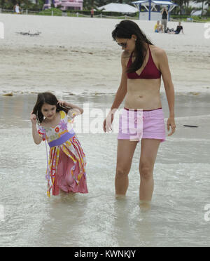 MIAMI BEACH, FL - JUNE 18: Katie Holmes and Suri Cruise had a fun day out on beach today in Miami, outside their hotel.  The famous mother and daughter pair played in the sand and splashed in the waves, entertaining themselves while Tom Cruise is busy filming the feature “Rock of Ages.”  Suri wasn’t quite prepared for the water, as she splashed around in a dress instead of a bathing suit. But, Katie Holmes rocked a red bikini, showing off a flat stomach and proving that she isn’t hiding a baby bump.   on June 18, 2011 in Miami Beach, Florida    People:  Katie Holmes Suri Cruise Stock Photo