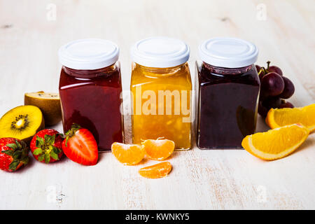 Three jars with jam on a wooden background. Delicious dessert and fresh fruits close-up. Stock Photo