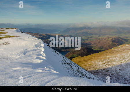 Winter scene of a snowy mountain ridge near Helvellyn in the English Lake District, with a glimpse of Thirlmere and Skiddaw on the horizon Stock Photo