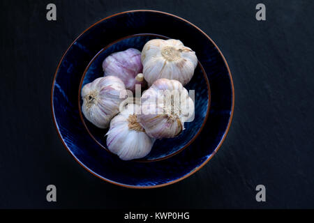 Garlic. Fresh garlic bulbs in vintage bowl over dark stone background. Top view on dark stone table. Stock Photo