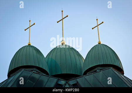 Three gold colored crosses on top of a green domed church roof isolated against a blue sky Stock Photo