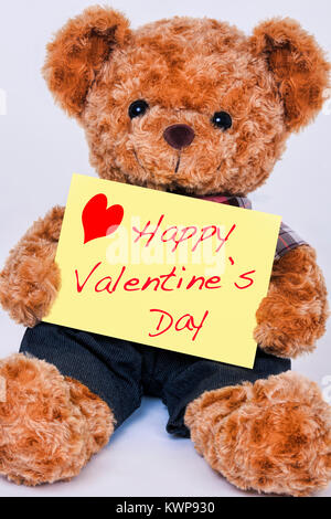 A cute teddy bear holding a yellow sign that says Happy Valentine's Day isolated on a white background Stock Photo