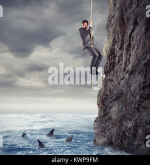 Businessman is likely to fall into the sea with sharks. concept of problems and difficulty in business Stock Photo