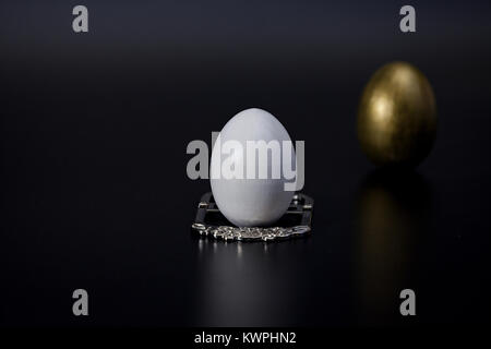 white egg on a silver stand in the foreground royal breakfast, black background blurred golden egg Stock Photo