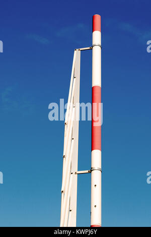 A typical red and white automatic access barrier in the up open position against a blue sky. Stock Photo