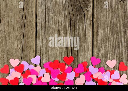 Colorful paper Valentines Day hearts forming a bottom border against rustic wood Stock Photo