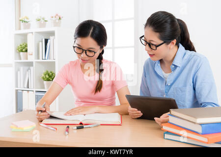 smiling elegant family teacher woman using mobile digital tablet to teach female student studying and preparing school exam. Stock Photo