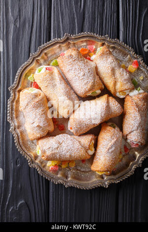 sweet cannoli stuffed with cheese cream and candied fruits close-up on a plate on a table. Vertical top view from above Stock Photo