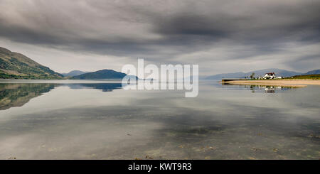 A house stands on a small peninsula, reflected in the calm sea on the shores of Loch Linnhe in the West Highlands of Scotland. Stock Photo