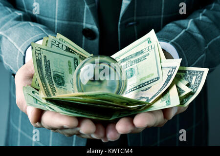 closeup of a young caucasian businessman wearing an elegant gray suit, with a pile of dollar bills and a crystal ball in his hands Stock Photo