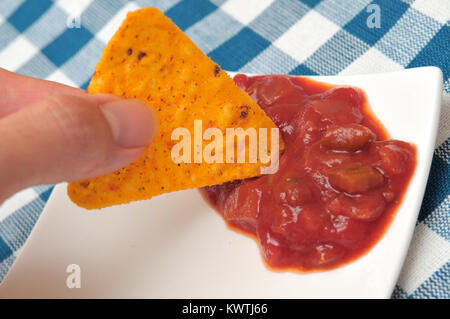 Dipping single tortilla chip into tomato sauce. Stock Photo