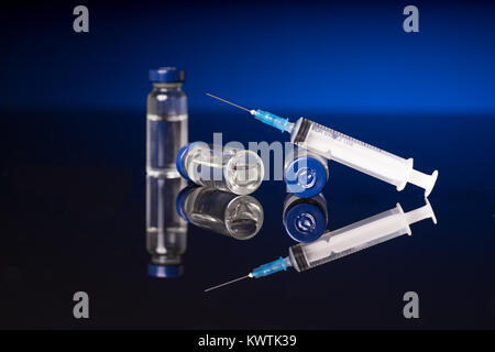 Syringe and medical vials isolated on black blue background with glossy reflection Stock Photo
