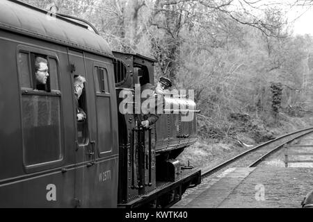Black & white photograph of engine driver leaning out of cab of vintage UK steam train, in action on Severn Valley Railway heritage line. Stock Photo