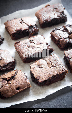 Double Chocolate Brownies. Homemade chocolate fudge brownies with chocolate chips on baking paper and black background. Stock Photo