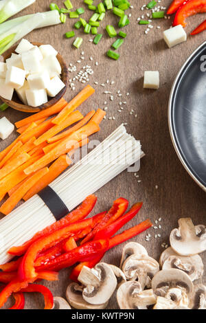 Vegetarian vegan asian food ingredients for stir fry with tofu, noodles, mushrooms and vegetables over wooden background with copy space. Stock Photo