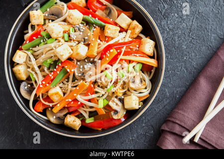 Stir fry with udon noodles, tofu, mushrooms and vegetables. Asian vegan vegetarian food, meal, stir fry in wok over black background, copy space. Stock Photo