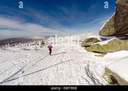 Running woman on winter trail, snow and white mountains. Young happy girl with backpack cross country running in mountains. Female trail runner joggin Stock Photo