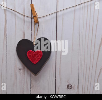 A single black heart with a smaller red heart in it's center hanging on a line in front of a white wooden fence Stock Photo