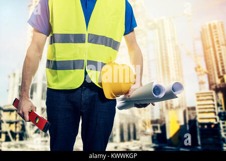 construction engineer with safety vest and blueprint rolls in hand at building site Stock Photo