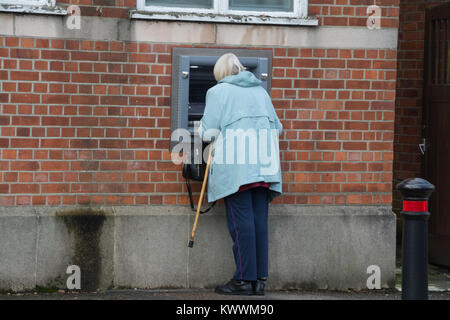 Elderly woman with a walking stick using an outdoor automatic teller machine (ATM, cash machine) at a bank Stock Photo