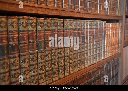 An antique and historical library containing many old leather-bound books from the 18th and 19th centuries, tightly stacked on shelves. Stock Photo