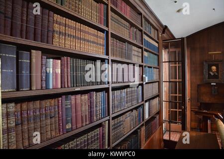 An antique and historical library containing many old leather-bound books from the 18th and 19th centuries, tightly stacked on shelves. Stock Photo