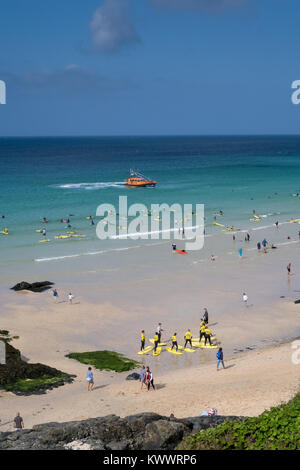 A summers day at St Ives beach in Cornwall. The RNLI lifeboat patrols offshore while surfers and tourists enjoys the beautiful sunny conditions. Stock Photo