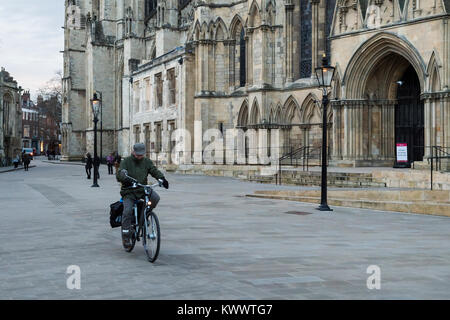 York centre - one elderly man riding a bike, cycles across piazza, past south entrance to magnificent York Minster   - North Yorkshire, England, UK. Stock Photo