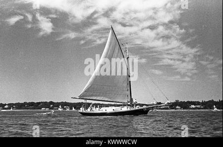 A gaff rigged sloop sailing off the shore of Nantucket Island,  Massachusetts, hauling a dingy behind, on a summer day. Stock Photo