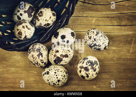 Several fresh eggs of a quail rolled out of the bascket on the wooden surface Stock Photo