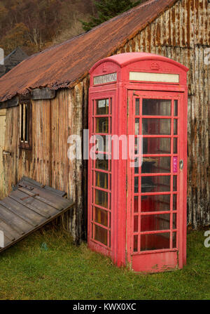 An old iconic red telephone box stands next to rusting huts in the village of Diabaig in the Torridon area of the Scottish Highlands Stock Photo
