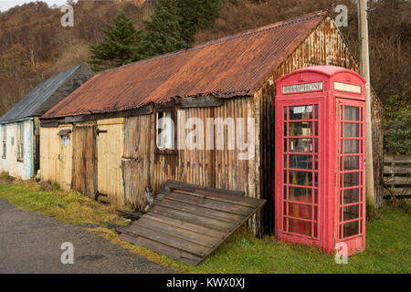 An old iconic red telephone box stands next to rusting huts in the village of Diabaig in the Torridon area of the Scottish Highlands Stock Photo