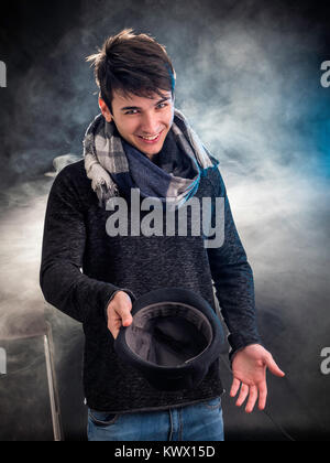 Cheerful young man posing and begging with hat in studio. Stock Photo