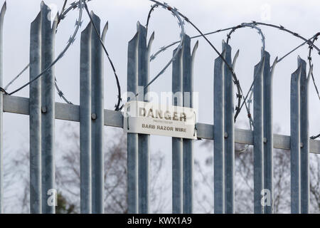 Galvanised steel spikes on top of a security gate or fence topped with barbed razor wire with a danger notice Stock Photo