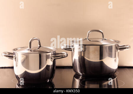 Cooking pots placed on modern electric ceramic stove. Reflections, closeup, details. Stock Photo