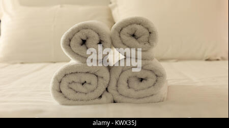 Hotel's bedroom. White fluffy, rolled towels, linen sheets and pillows on a tidy bed. Closeup. Stock Photo
