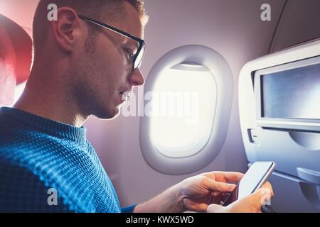 Connection in the airplane. Young passenger (traveler) using smart phone during flight. Stock Photo