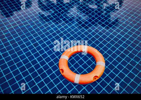 Orange lifebuoy floating on the water surface of the swimming pool against reflection of the palm trees. Stock Photo
